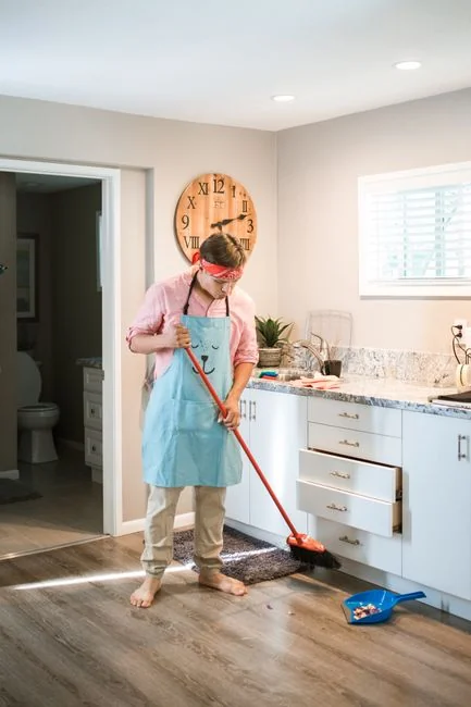 A young, attractive woman is cleaning the living room and mopping the floor while doing housework. A beautiful loft-style apartment with modern furniture and green plants can be seen.